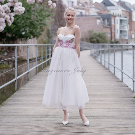 Model wearing strapless floral midi wedding dress with tulle skirt, standing outdoors in natural light
