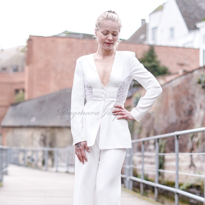 Mannequin portant un costume couture blanc avec pantalon et blazer long à basque, décoré de détails brodés à la main. Mannequin portant un costume couture blanc avec pantalon et blazer long à basque, décoré de détails brodés à la main.