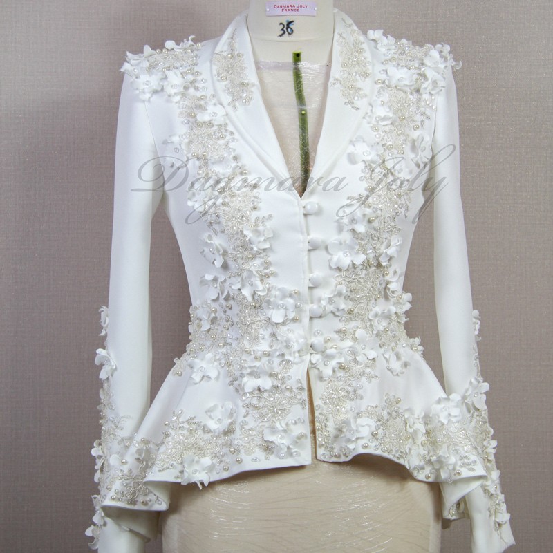 Gros plan sur les détails couture : appliqués floraux, boutons nacrés et dentelle délicate sur un tailleur de mariée.