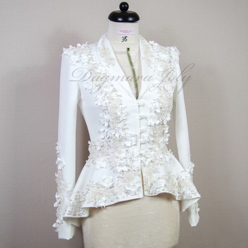 Gros plan sur les détails couture : appliqués floraux, boutons nacrés et dentelle délicate sur un tailleur de mariée.