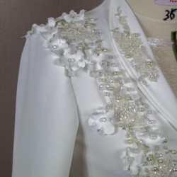 Gros plan sur les détails couture : appliqués floraux, boutons nacrés et dentelle délicate sur un tailleur de mariée.
