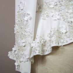 Gros plan sur les détails couture : appliqués floraux, boutons nacrés et dentelle délicate sur un tailleur de mariée.