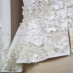 Gros plan sur les détails couture : appliqués floraux, boutons nacrés et dentelle délicate sur un tailleur de mariée.