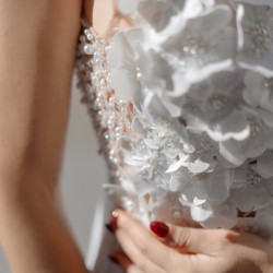 Close-up of delicate handcrafted flowers and pearl embellishments on the couture wedding dress, showcasing artisanal detailing.