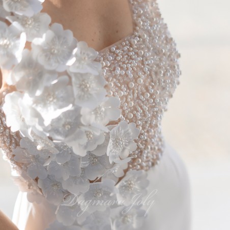Zoom sur les ornements en perles et les fleurs faites main sur la robe de mariée artisanale.