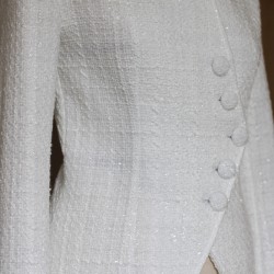 Zoom sur le tissu de la veste de mariée blanche asymétrique en tweed montrant le tweed texturé et les coutures