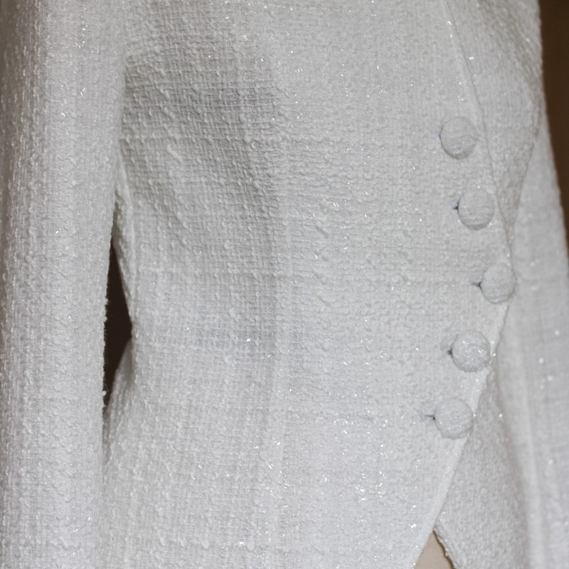 Zoom sur le tissu de la veste de mariée blanche asymétrique en tweed montrant le tweed texturé et les coutures
