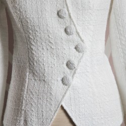 Zoom sur le tissu de la veste de mariée blanche asymétrique en tweed, montrant le tweed texturé et les coutures