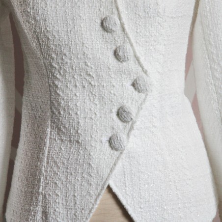 Close-up of women's white bridal asymmetrical tweed jacket fabric showing textured tweed and stitching.