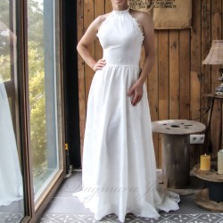 Femme dans la chambre dans une élégante robe de mariée fabriquée en France, à ourlet asymétrique et traîne.