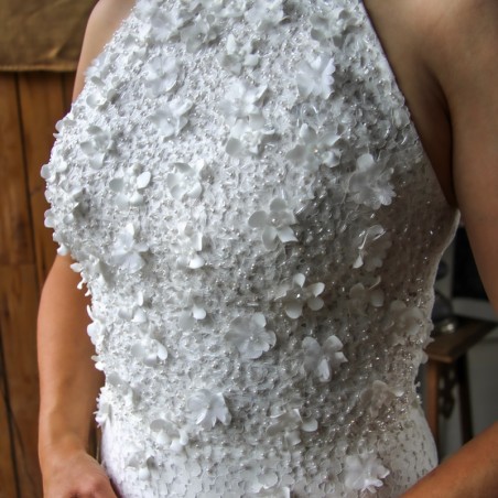 Close-up of hand-cut flower appliqués, pearls, and transparent shiny tubes on the bodice of a lace wedding dress.