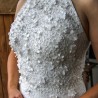 Close-up of hand-cut flower appliqués, pearls, and transparent shiny tubes on the bodice of a lace wedding dress.