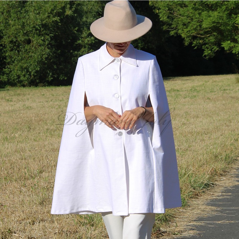 Model wearing a white swing-style bridal cape with silver buttons and a turndown collar Model wearing a white swing-style bridal cape with silver buttons and a turndown collar