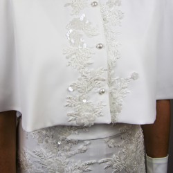Gros plan sur la broderie perlée faite main d’une cape de mariée en crêpe.
