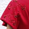 Gros plan sur la broderie florale artisanale sur le manche du manteau rouge en laine.