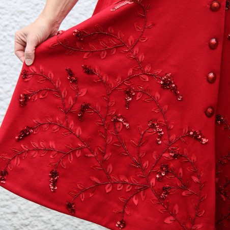 Gros plan sur la broderie florale artisanale devant du manteau rouge en laine.