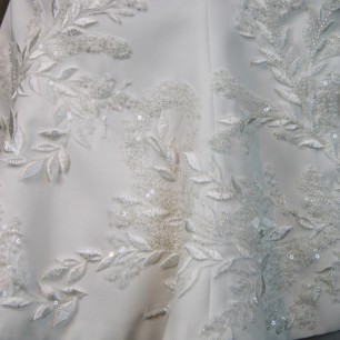 Gros plan sur les broderies couture d’un tailleur de mariée fait main