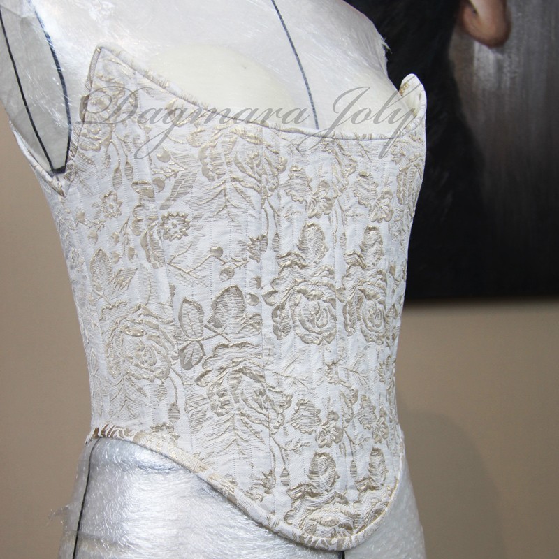 Photo en lumière tamisée soulignant la brillance et la richesse du tissu en brocart de ce corset