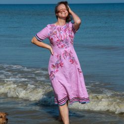 Femme portant une robe midi en lin violette avec manches courtes et broderies faites main, debout en extérieur