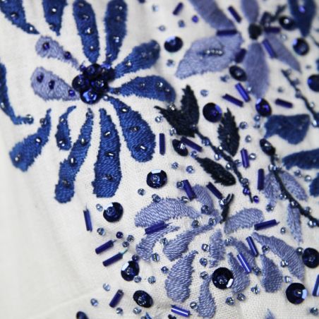 Zoom of hand-embroidered motifs on a white linen sleeveless dress,