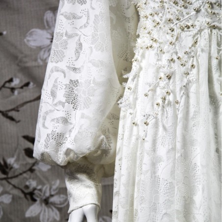 Gros plan sur la dentelle florale du devant de la robe, finement brodée à la main avec des perles nacrées