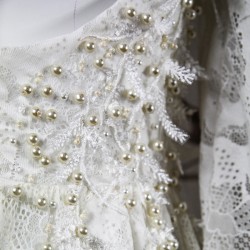 Gros plan sur la dentelle florale du devant de la robe, finement brodée à la main avec des perles nacrées