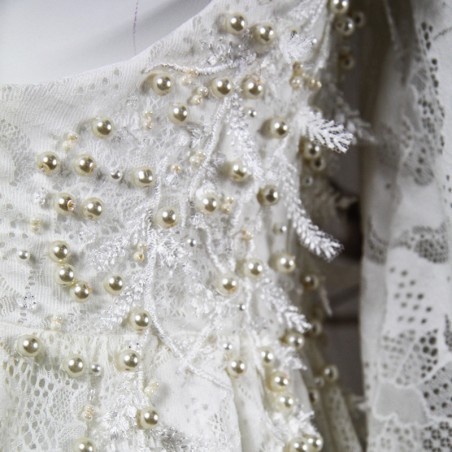 Gros plan sur la dentelle florale du devant de la robe, finement brodée à la main avec des perles nacrées
