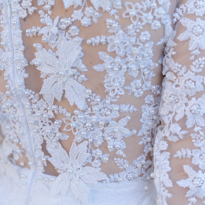 Detailed view of lace fabric and 3/4 sleeve with hand-sewn pearls and floral design