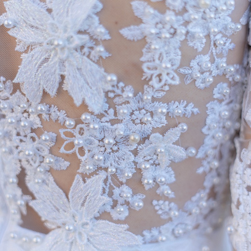 Close-up of hand-embellished floral appliqués and pearl details on lace wedding gown