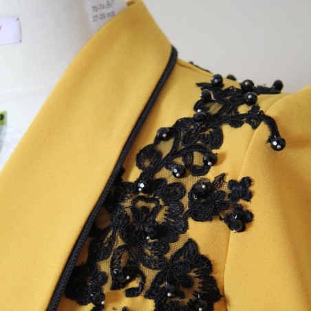 Gros plan sur la dentelle et les perles noires d’une veste de soirée moutarde